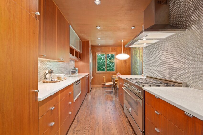 Modern kitchen with wooden cabinets, stainless steel appliances, and a large window offering natural light and outdoor view.