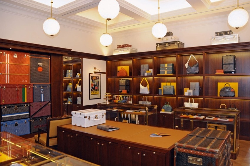 Luxury boutique interior with wooden shelves displaying various high-end luggage and handbags, elegant lighting above.