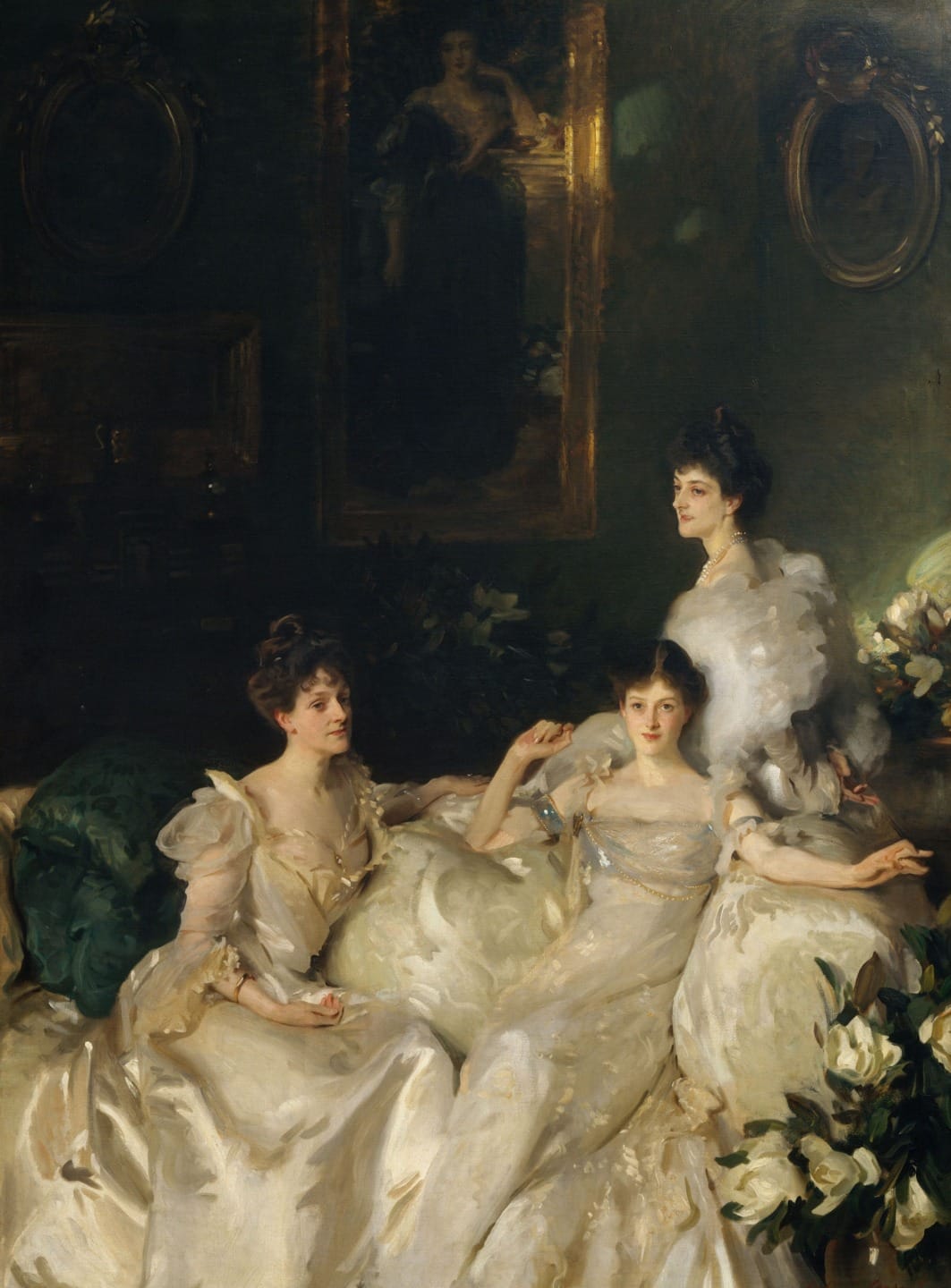 Three women in elegant white dresses sit and stand in a dimly lit, opulent room with a large mirror and floral decor.