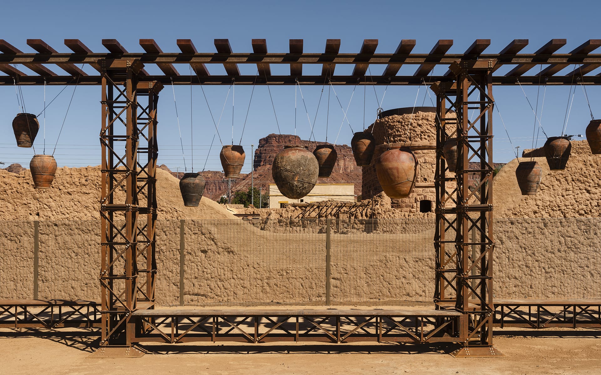 Outdoor art installation with hanging clay pots against a desert landscape and clear blue sky in the background.