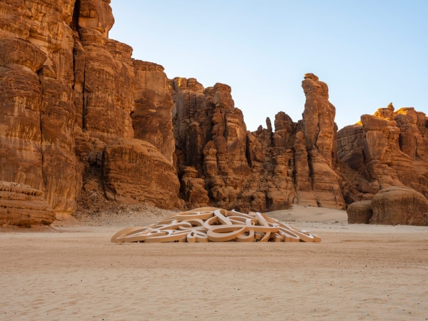 Modern art installation in a desert landscape with towering rock formations under a clear blue sky.