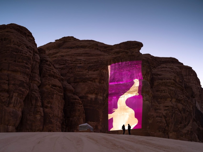Two people admire a vibrant digital display projected on a large rock formation at dusk.