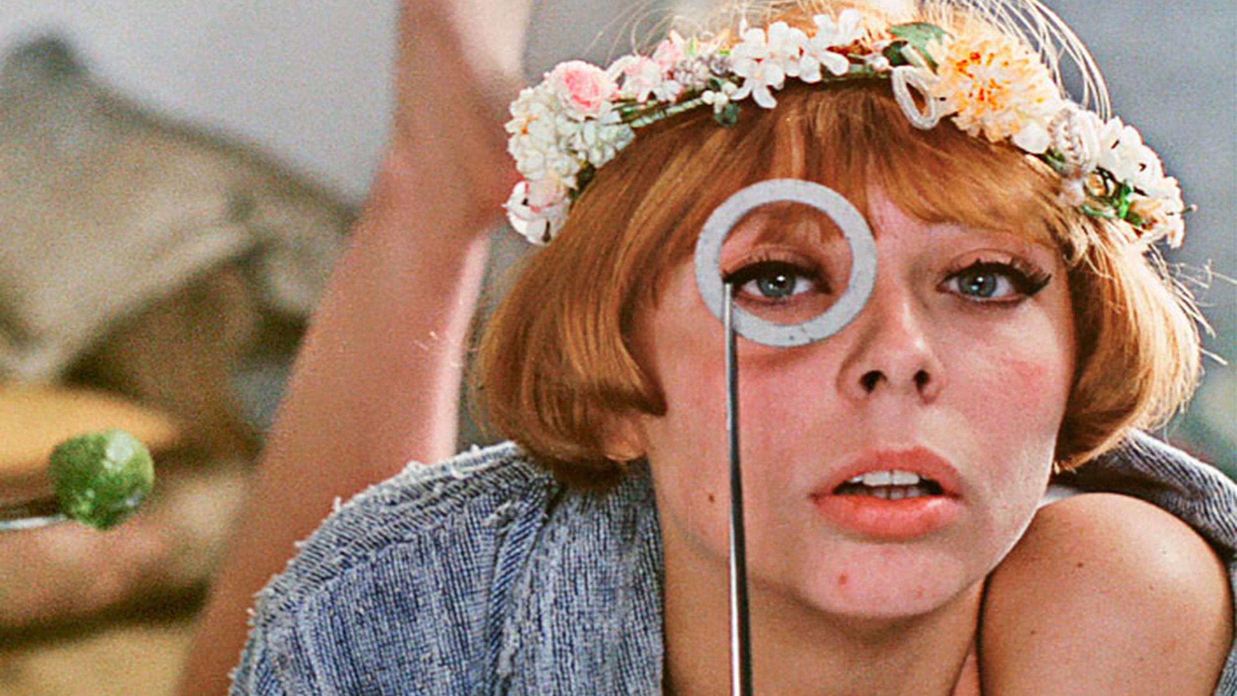 Woman wearing a flower crown looking through a circular object with playful expression.