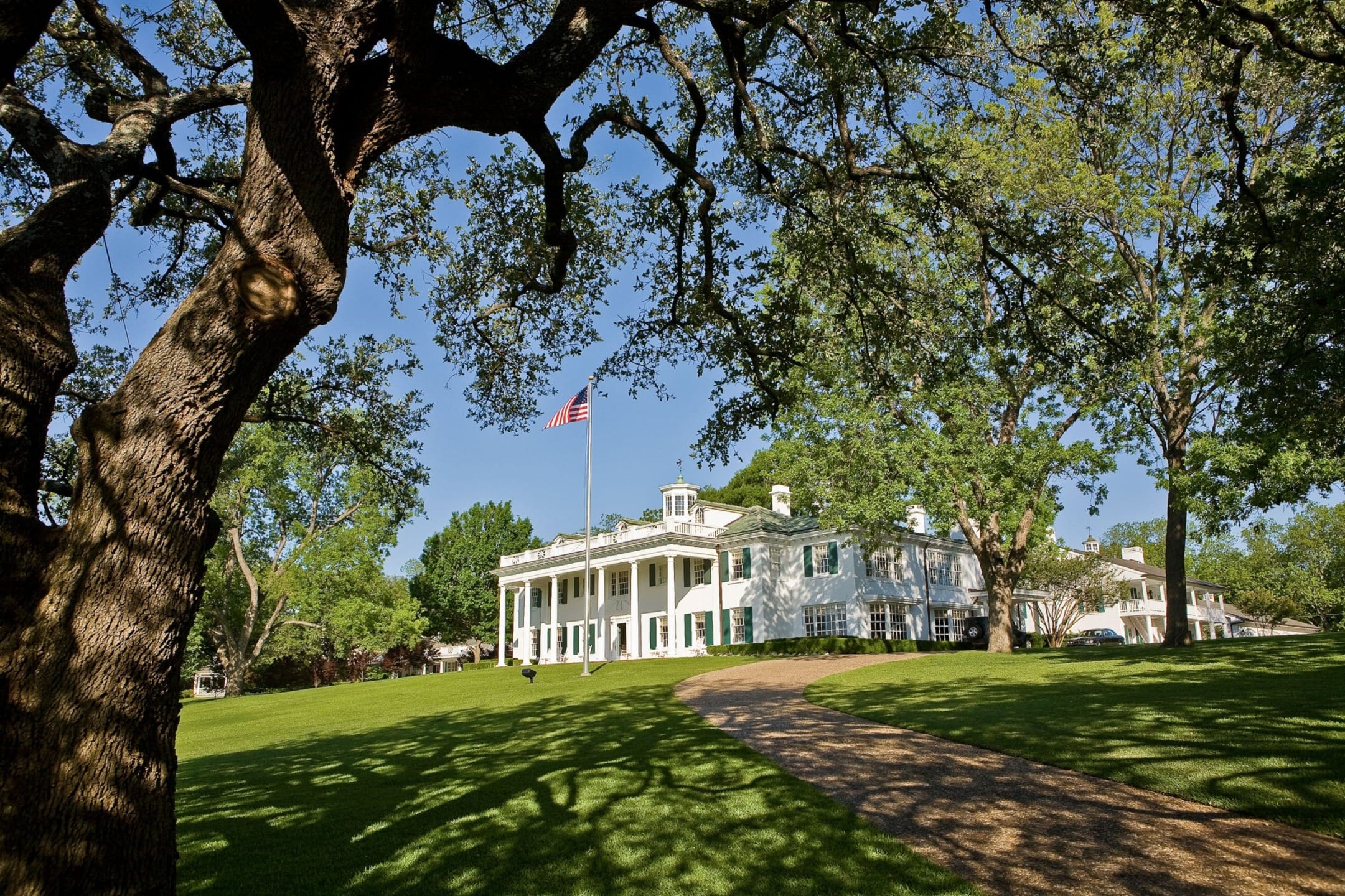 Historic plantation house with an American flag, surrounded by trees and a curved path leading through a lush green lawn.
