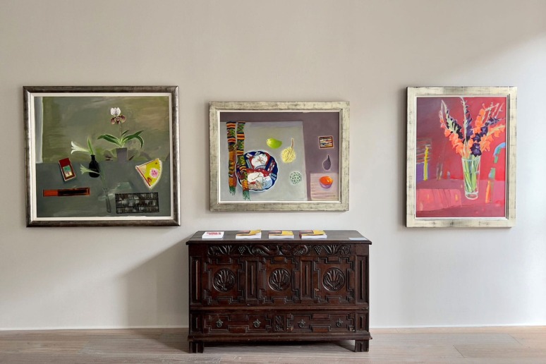 Three colorful abstract paintings hanging above a vintage wooden chest against a neutral wall.