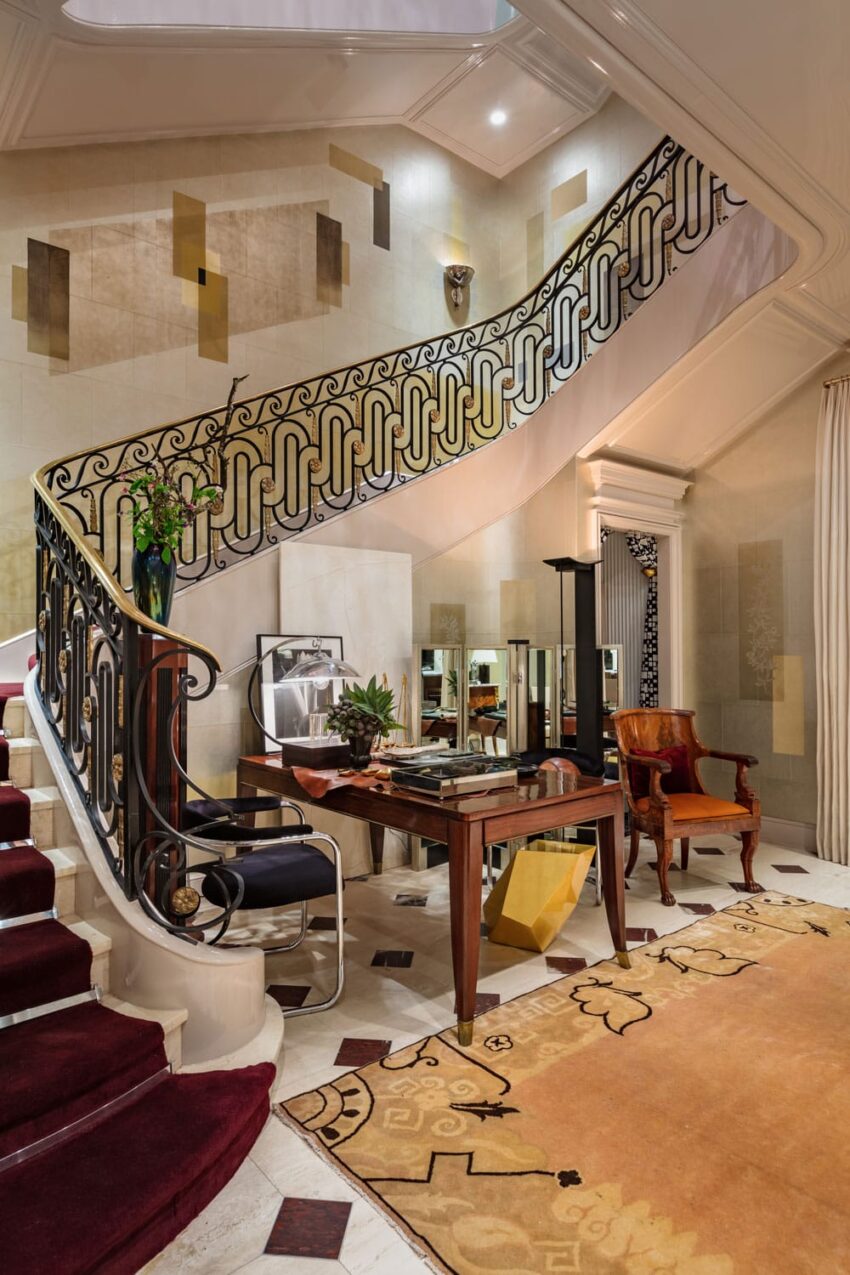 Elegant interior with ornate staircase, modern furniture, and decorative rug in a luxurious, art deco style room.
