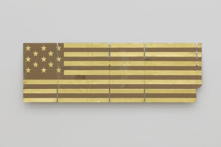 Abstract American flag artwork with gold stripes and stars on a segmented background displayed on a white wall.