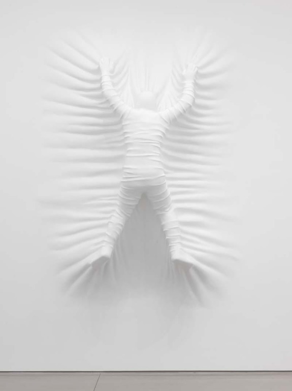 Sculpture of a figure pressing against white fabric from the other side, creating a 3D effect on a flat surface.