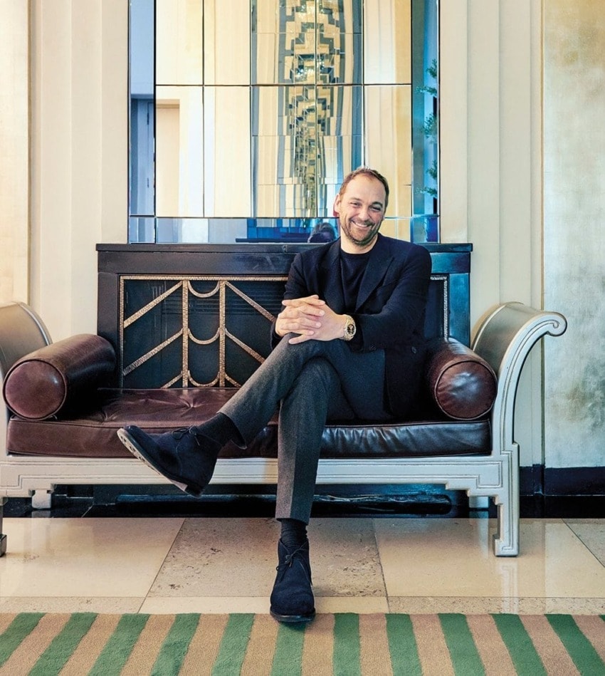 Person sitting on a stylish brown couch in an elegant room with a striped rug and decorative mirrors in the background.