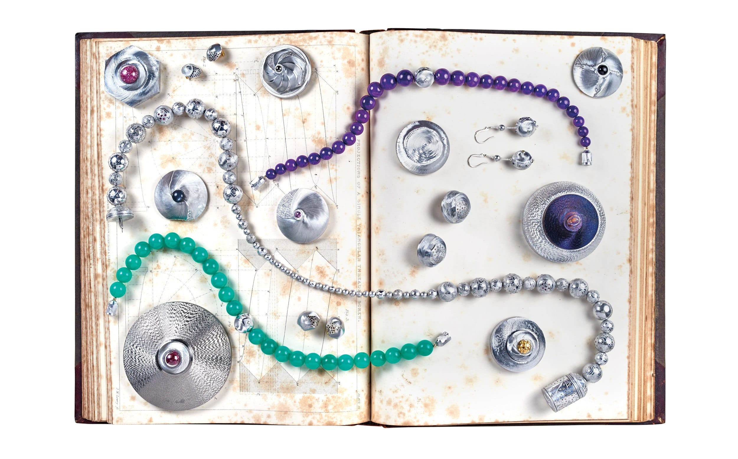 Open book with scattered silver trinkets, jeweled beads in green, purple, and silver, creating a whimsical art display.