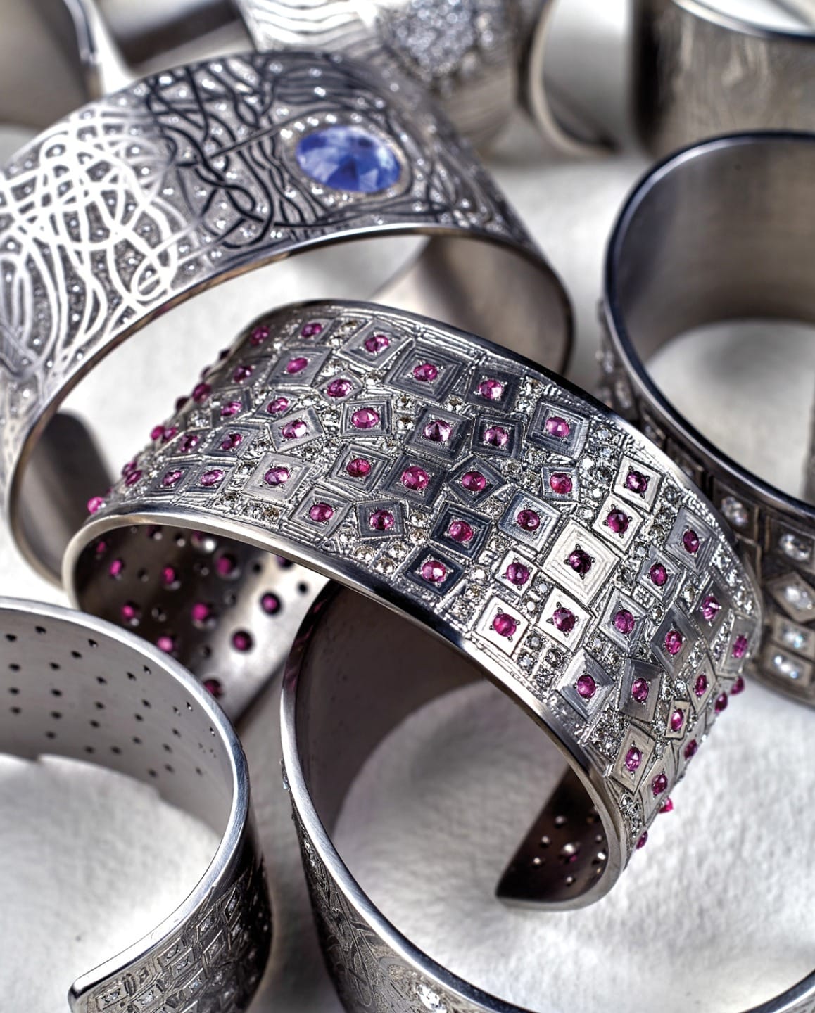 Silver bracelets adorned with pink gemstones and intricate designs arranged on a white surface.
