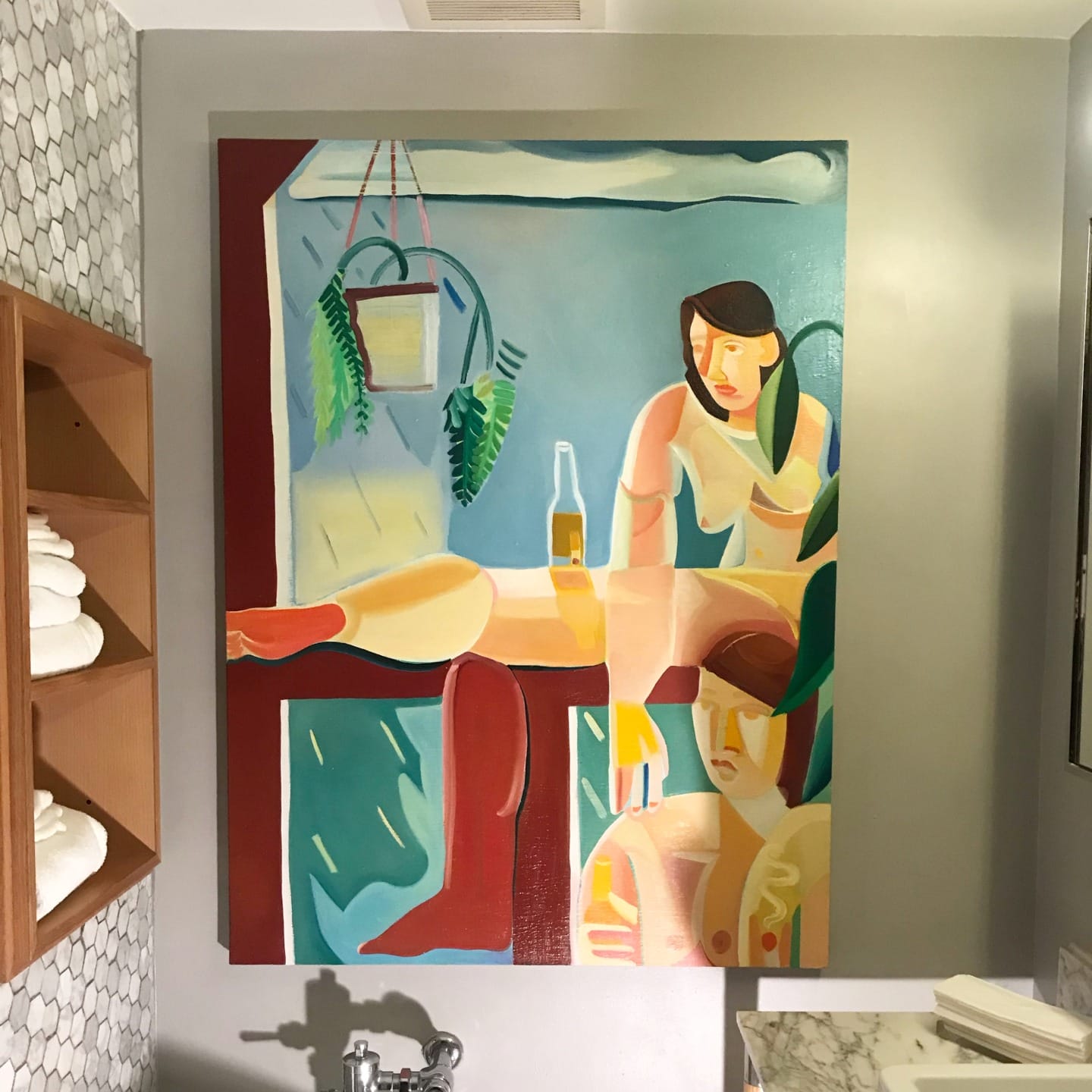 colorful abstract painting featuring figures and a bottle, hung in a modern bathroom with towels and a hexagonal tile wall
