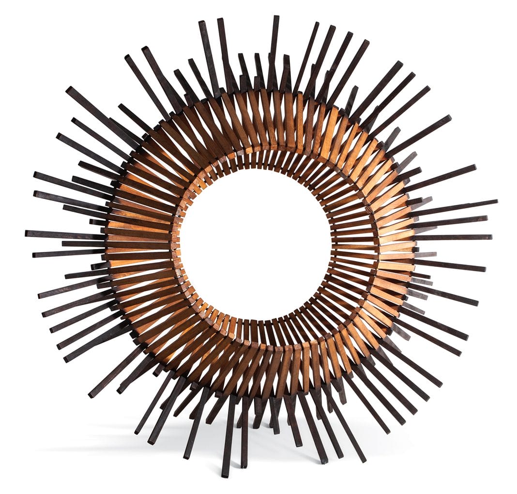 Wooden circular sculpture with radiating spikes creating a dynamic sunburst effect, made of dark and light brown wood.