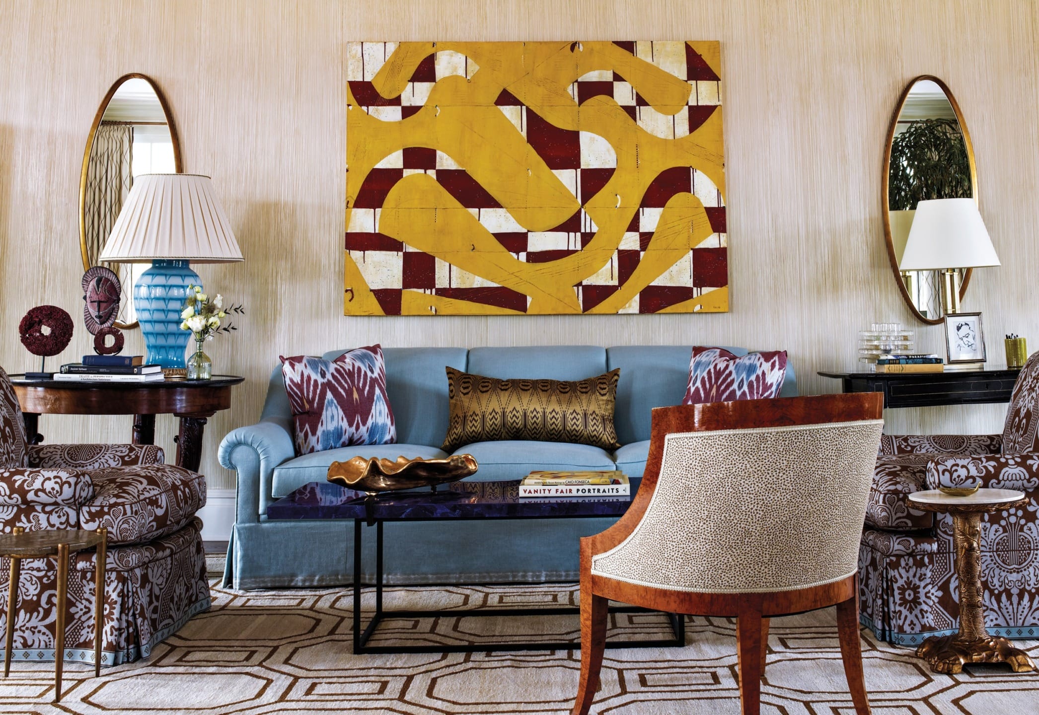 Elegant living room with a blue sofa, patterned chairs, abstract yellow wall art, and decorative items on side tables.