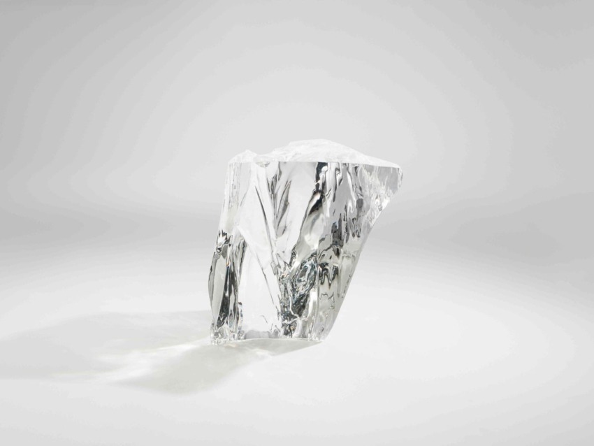 A large, clear quartz crystal standing upright on a smooth, white surface with soft lighting and subtle shadows.