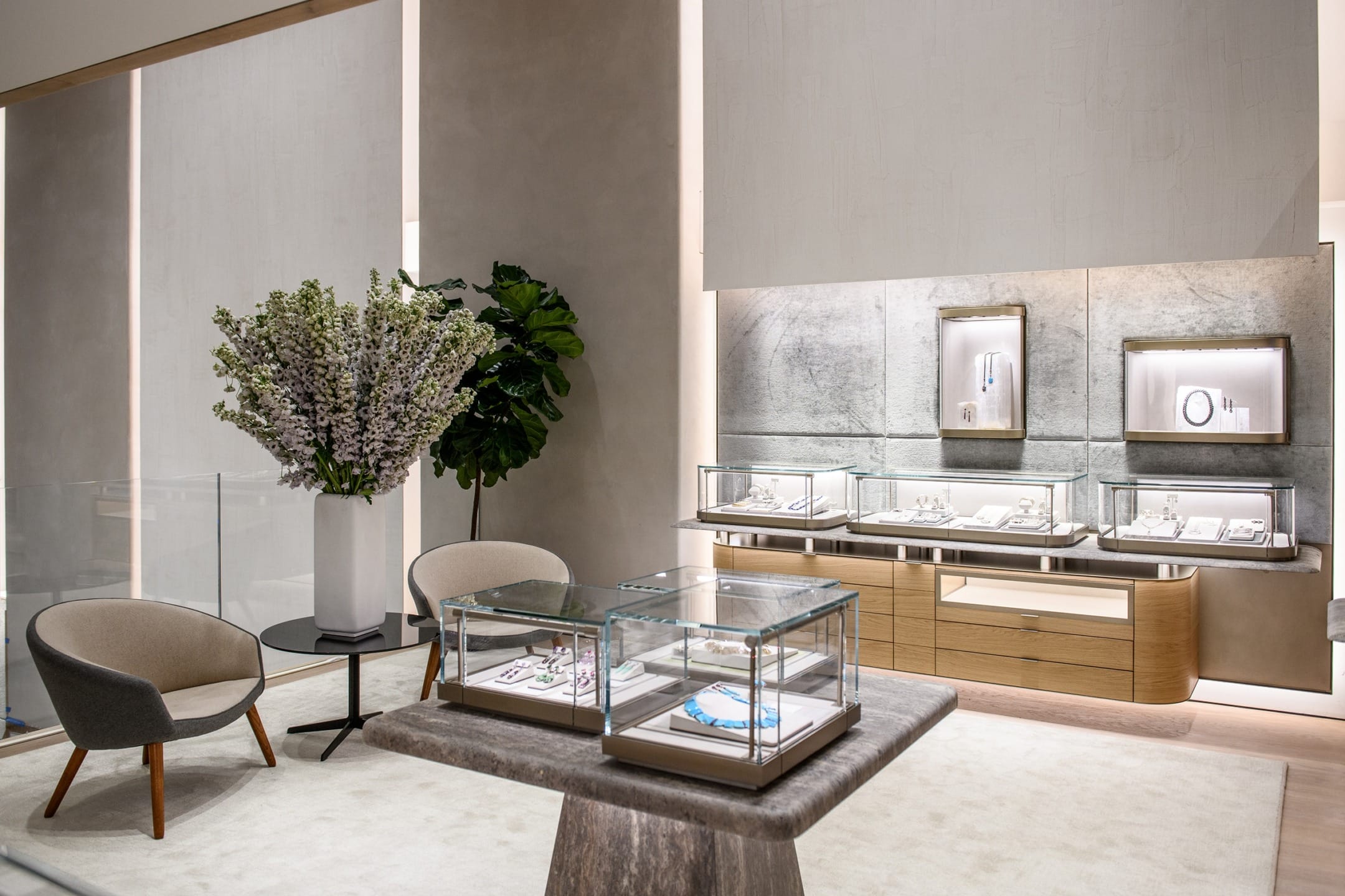 Modern jewelry store interior with display cases showcasing jewelry, elegant seating area, and decorative plants.