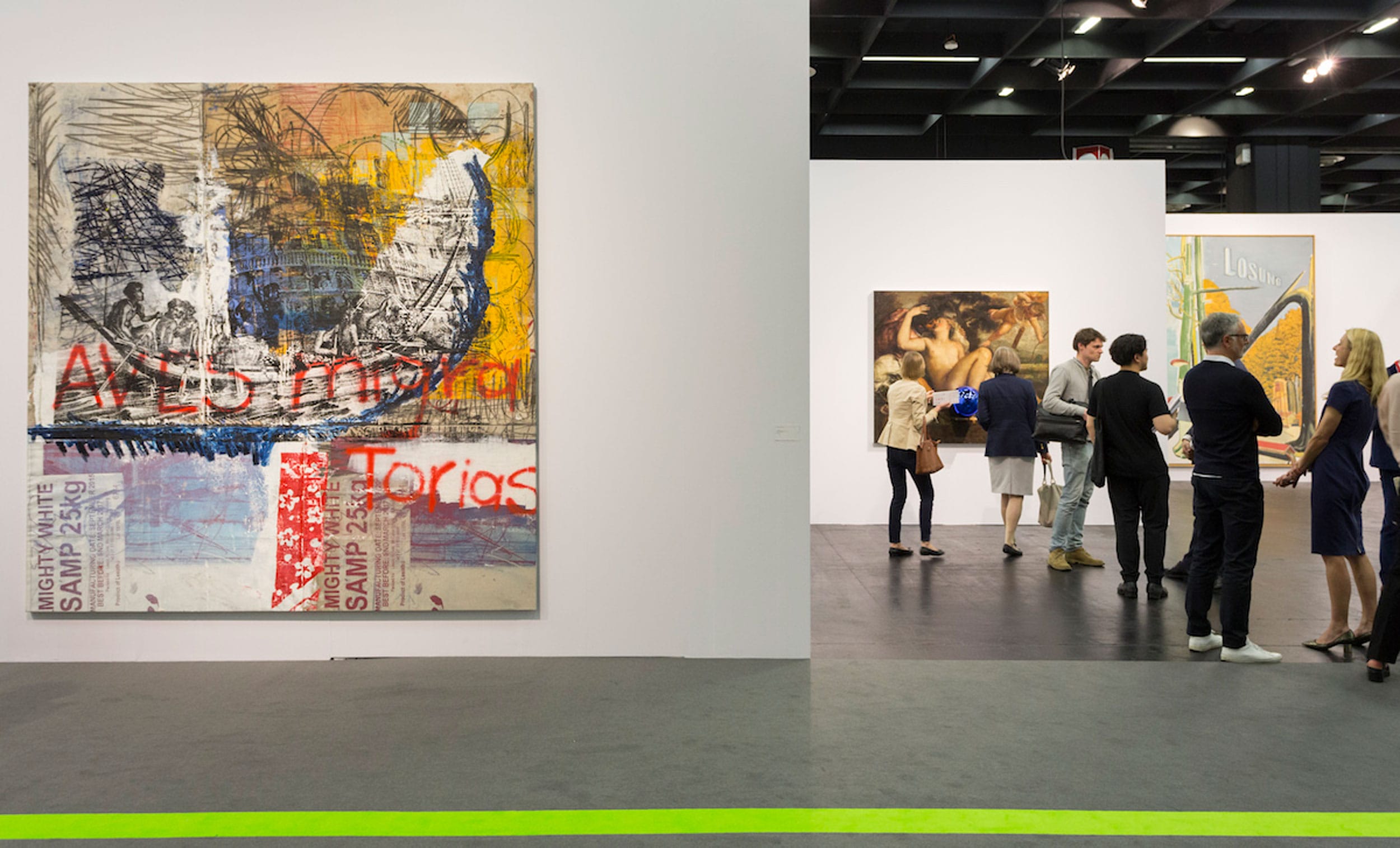 People viewing modern art paintings in a gallery setting, with large abstract artwork prominently displayed on white walls.