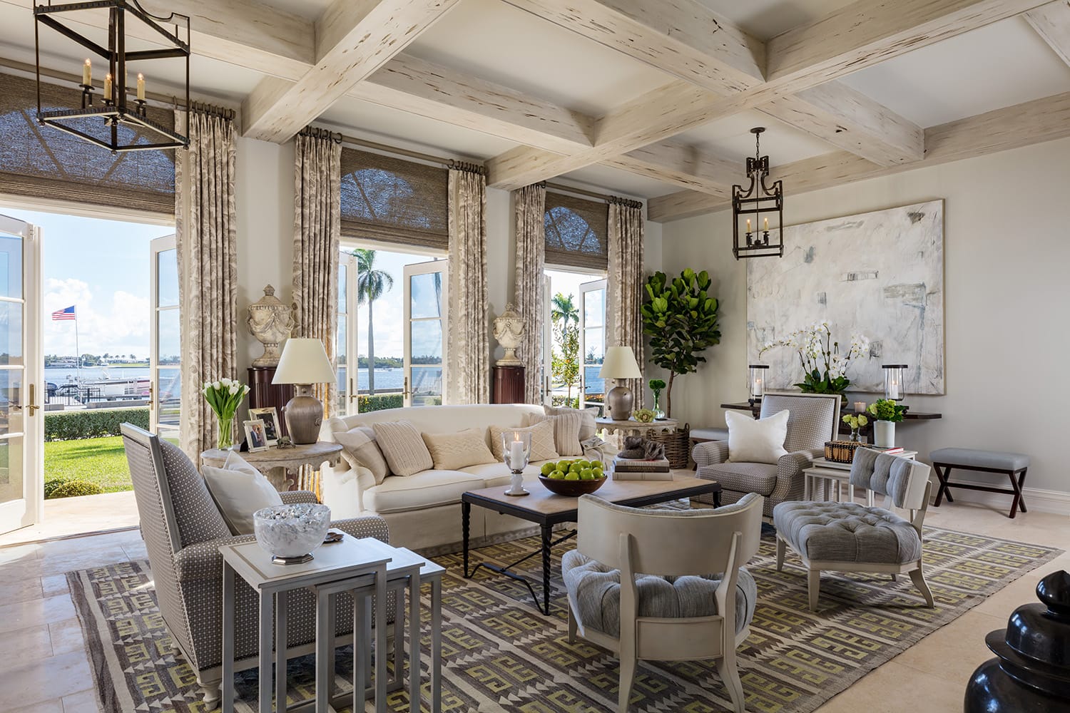 Luxurious living room with cream sofas, large windows, patterned rug, and greenery, overlooking a waterfront view.