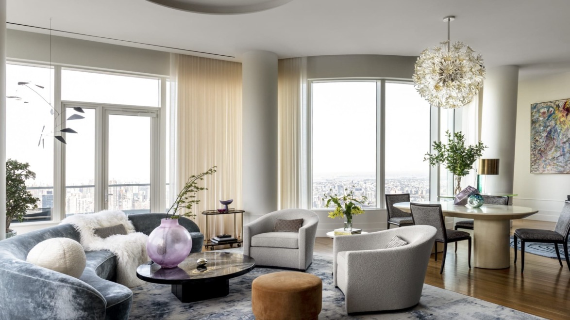 Modern living room with large windows, stylish furniture, round table, unique chandelier, city view, and decorative plants.