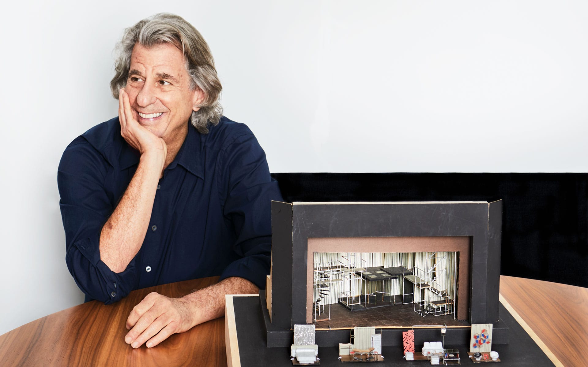 Person smiling while sitting at a table, looking at a small architectural model featuring various materials and designs.