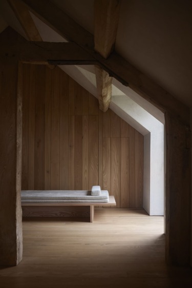 Minimalist wooden room with angled ceiling, featuring a simple bench and soft lighting.