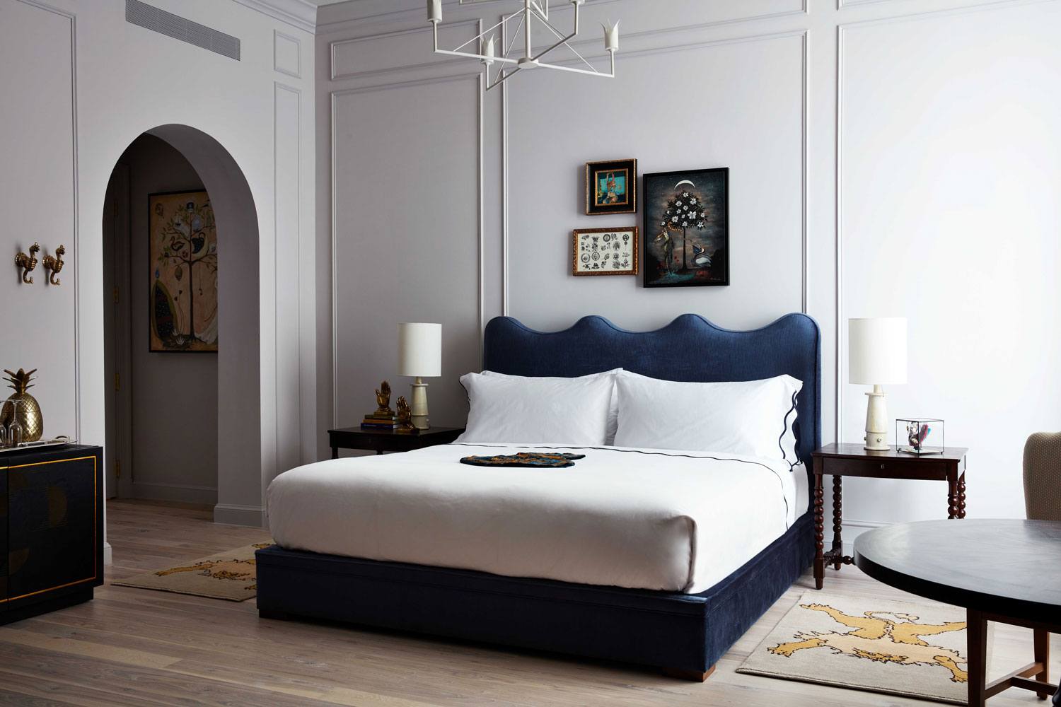 Stylish bedroom with a navy blue upholstered bed, white linens, and minimalist decor in a modern, light-filled space.