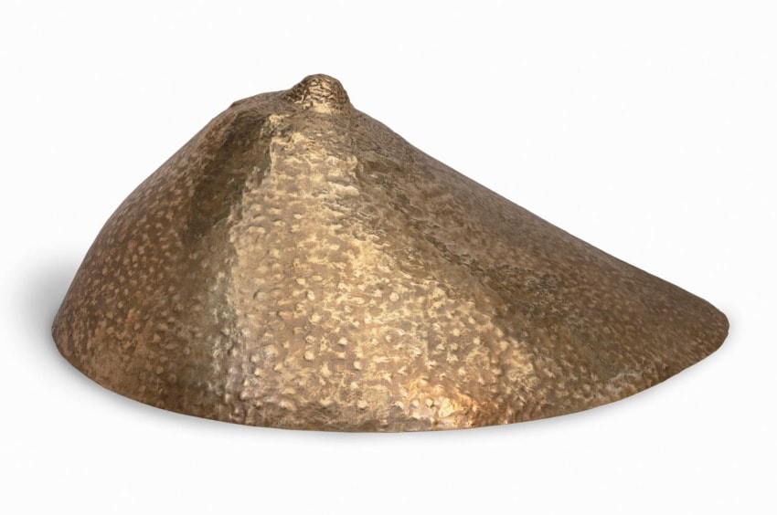 Bronze breastplate from ancient armor with textured surface and conical shape.