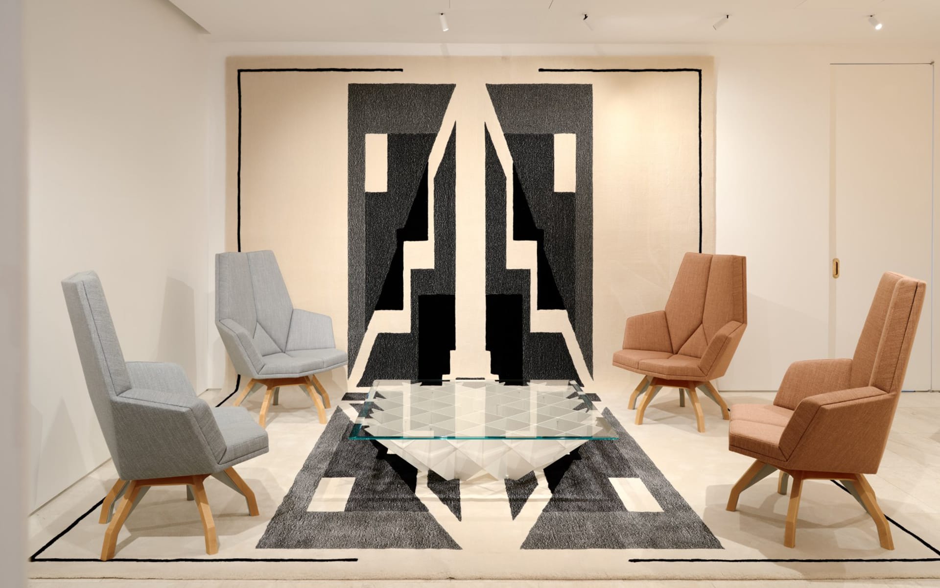 Modern lounge with geometric black-and-white rug, glass table, and four angled armchairs in a bright, minimalist space.