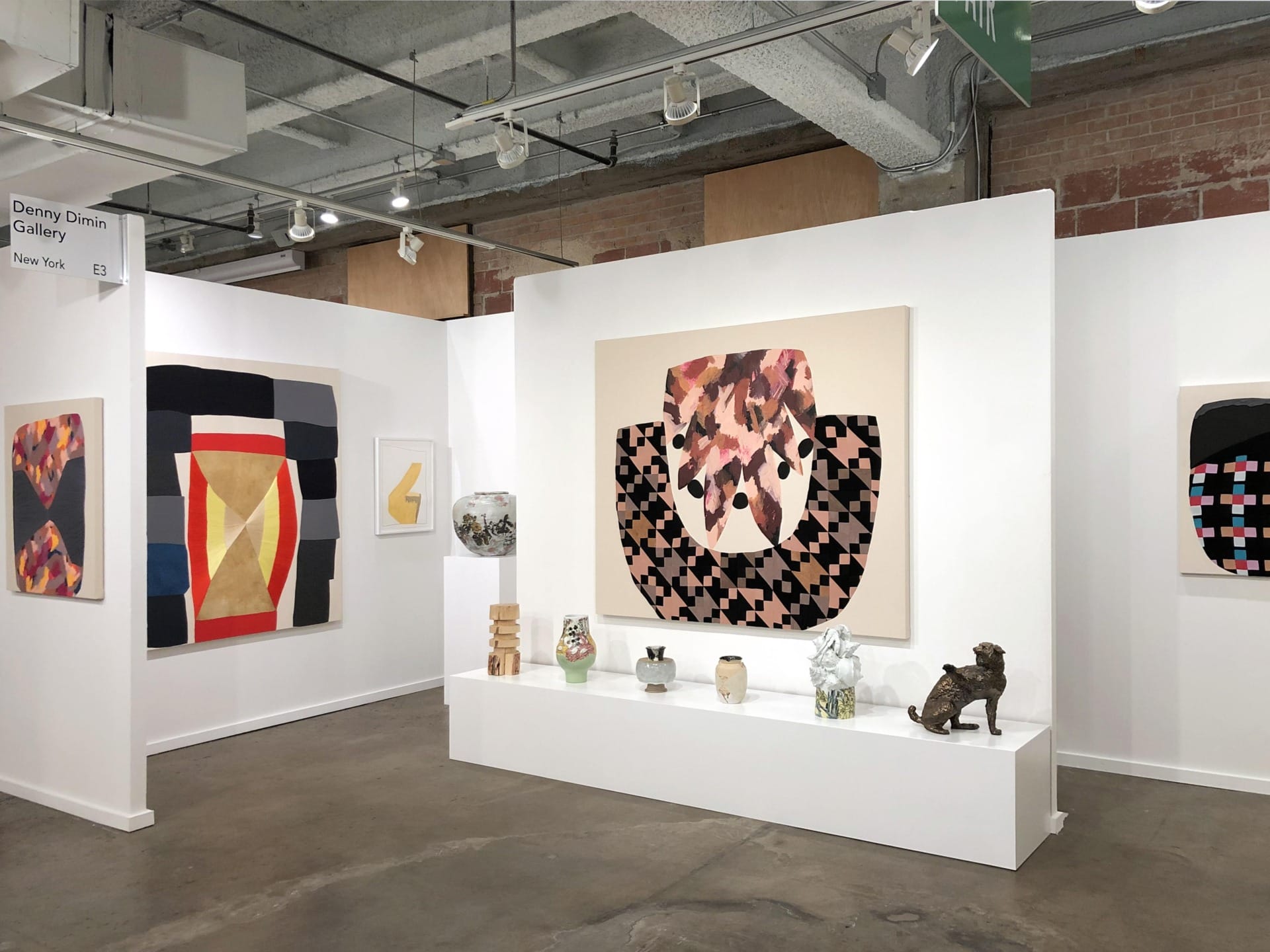 Art gallery exhibition with colorful abstract paintings and sculptures displayed on white walls and pedestals.