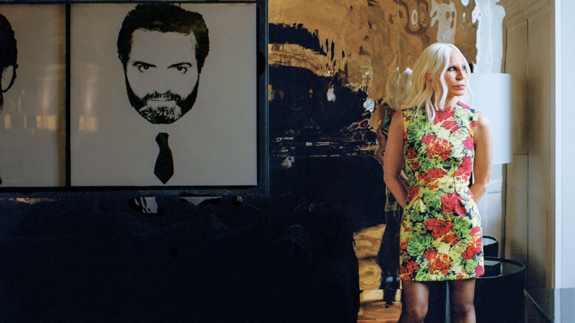Person in a colorful floral dress standing beside an abstract black-and-white artwork on a wall.