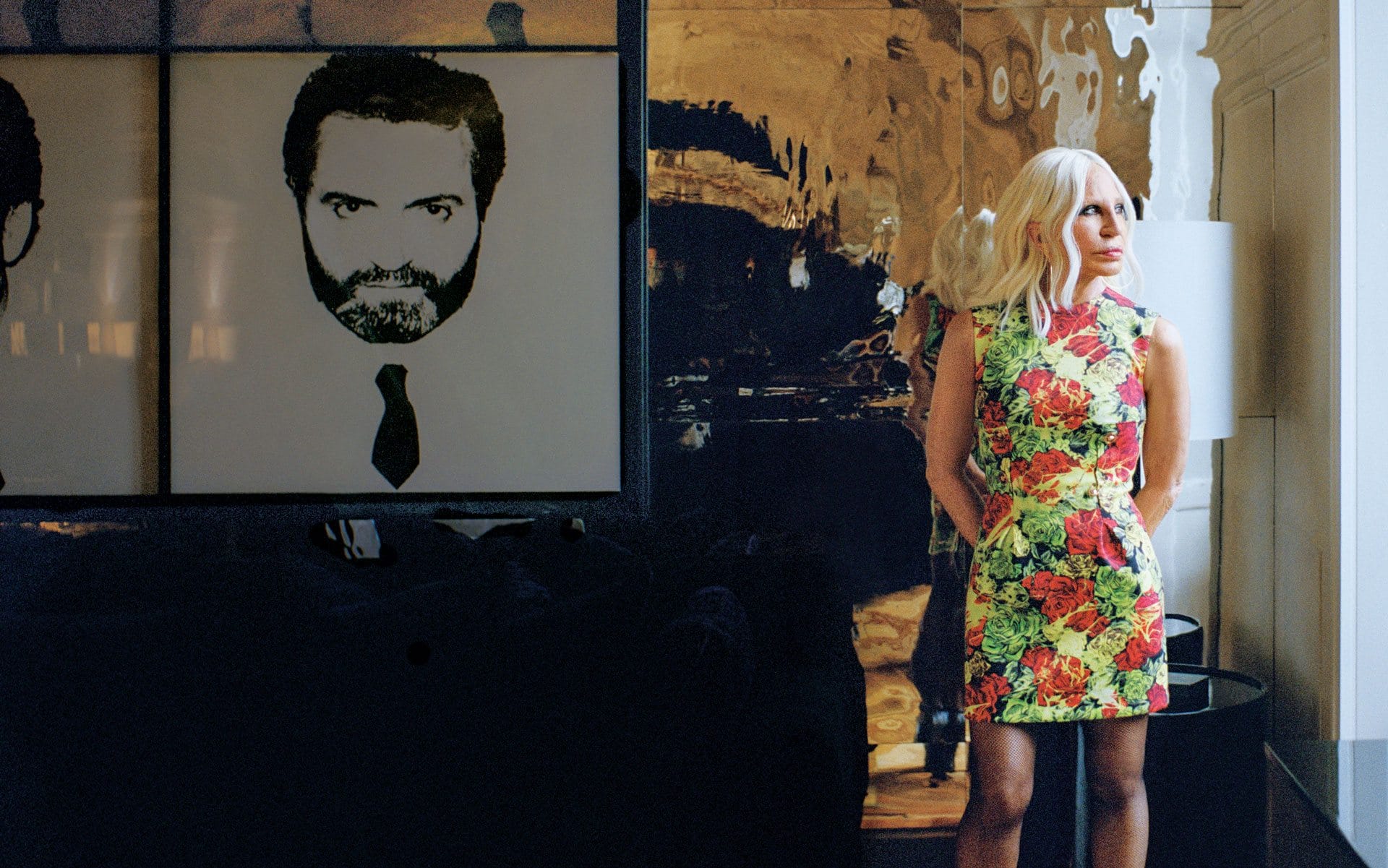 Person in a colorful floral dress standing beside an abstract black-and-white artwork on a wall.