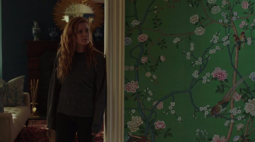 Person standing by a doorway in a dimly lit room with vibrant floral wallpaper on the wall.