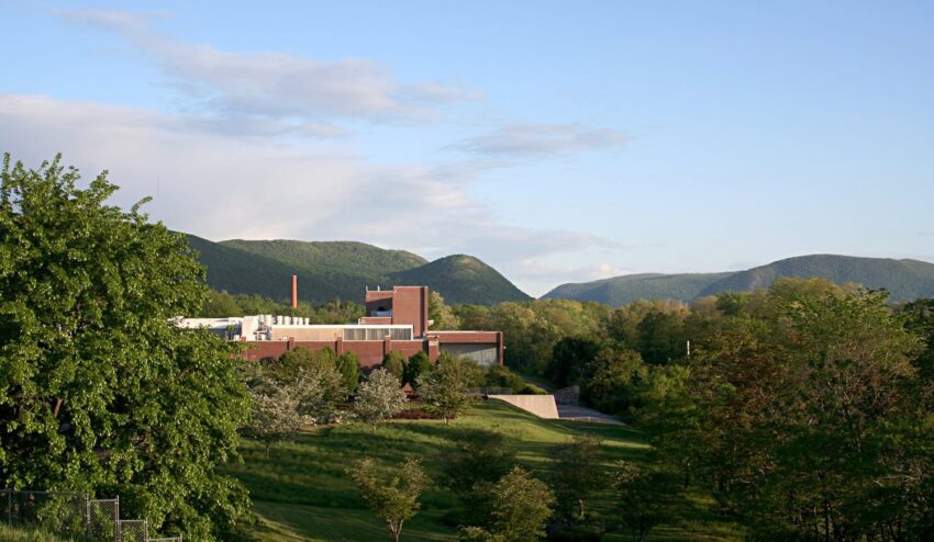 Scenic view of a large building surrounded by lush greenery and distant green mountains under a blue sky.