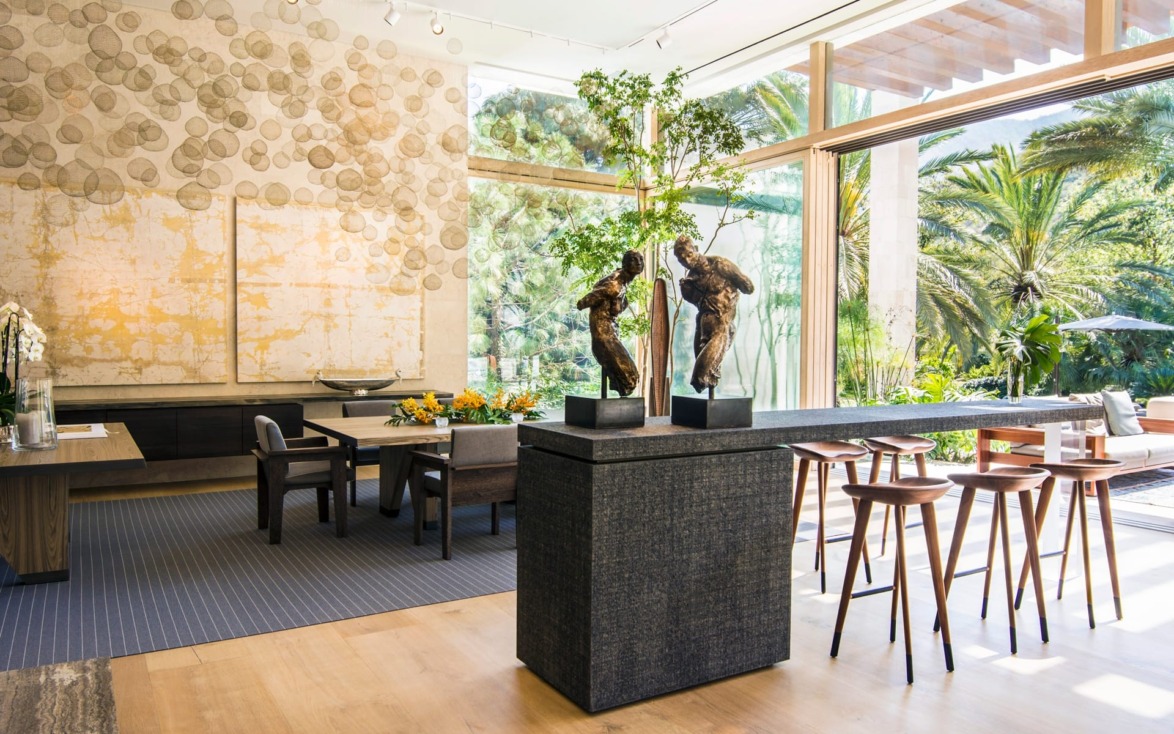 Spacious modern dining area with large windows, artistic sculptures, and wooden chairs overlooking a lush garden.
