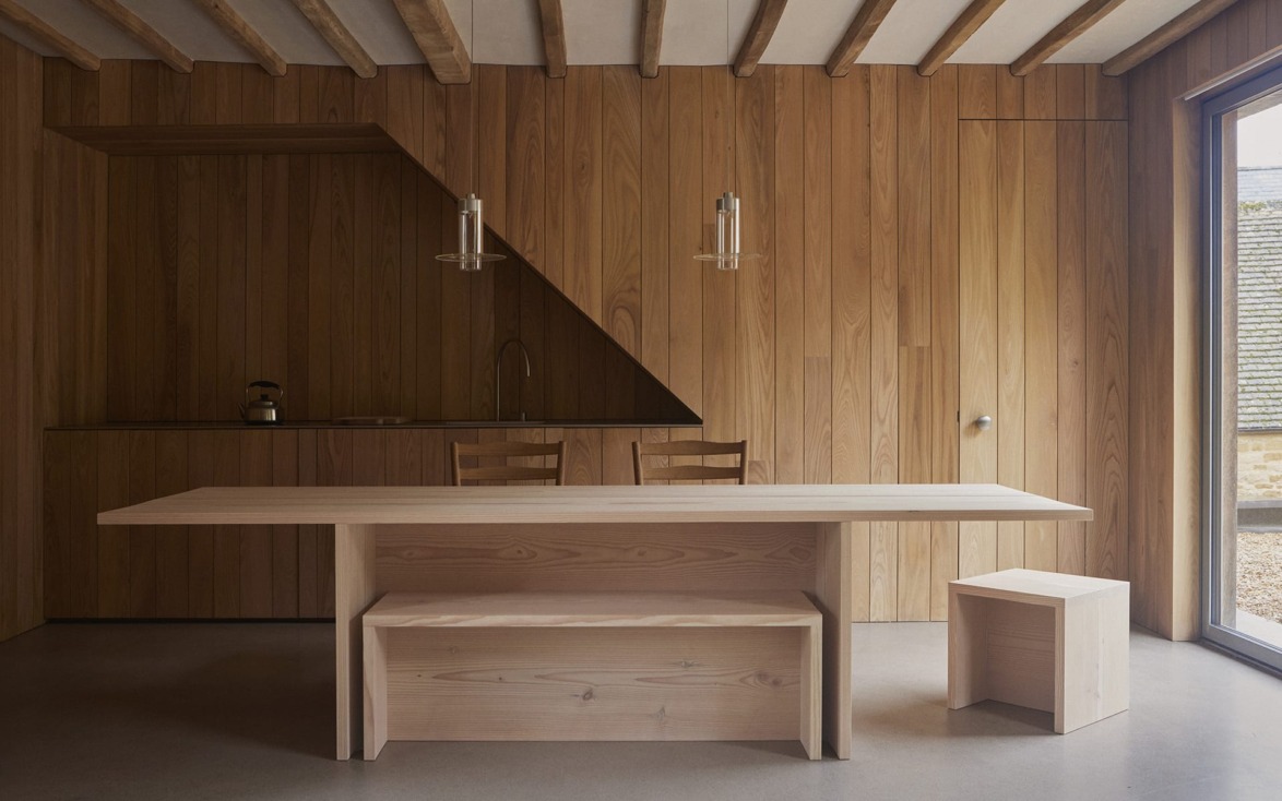 Minimalist wooden dining area with table, chairs, pendant lights, and a built-in kitchen in a modern, wood-paneled room.