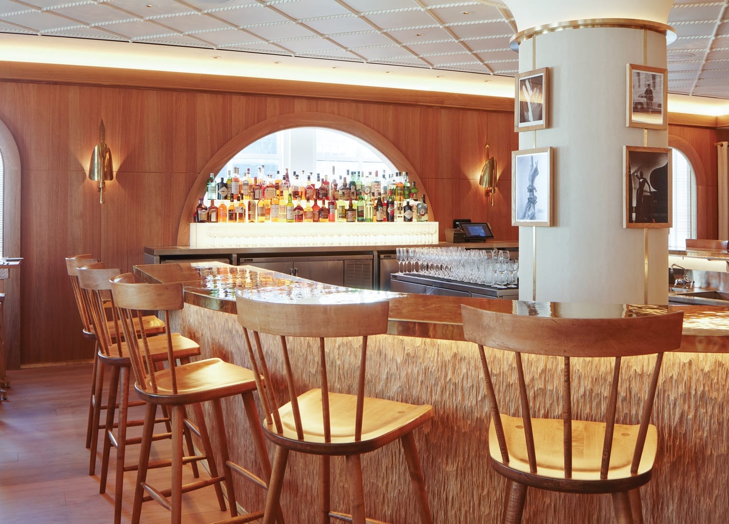 Cozy and elegant bar interior with wooden stools, a polished counter, and a wide selection of spirits on display.