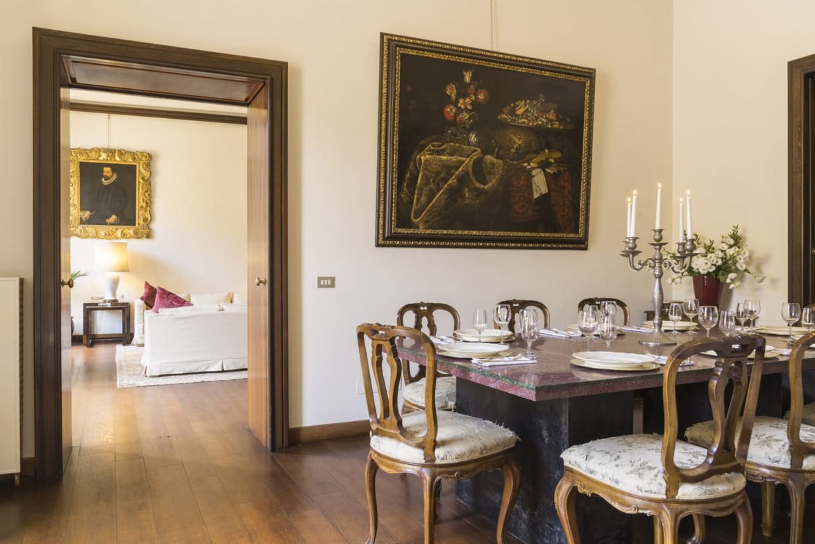 Elegant dining room with a large table set for guests, vintage chairs, and classic paintings on cream-colored walls.
