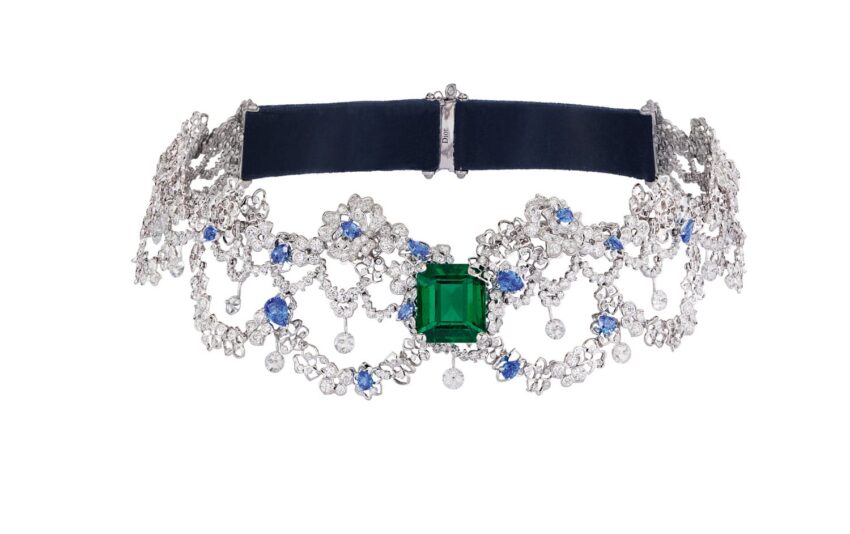 Ornate diamond choker necklace with a large green gemstone and blue accents set on a dark band.
