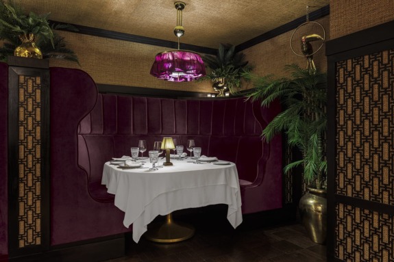 Luxurious restaurant booth with elegant maroon seating, a table set for four, and ambient lighting under a purple chandelier.