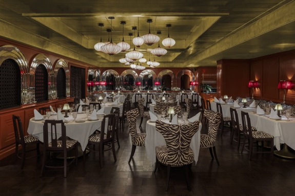 Elegant restaurant interior with zebra-patterned chairs, white tablecloths, and modern pendant lights.