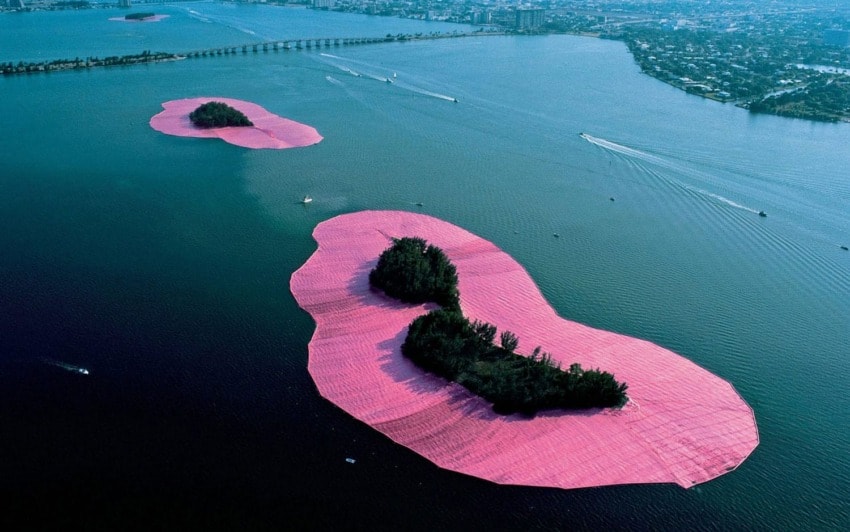 Two islands in a lake are surrounded by bright pink fabric, with a city visible in the background.