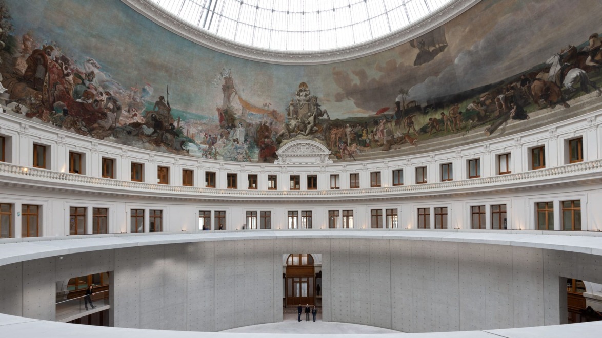 Interior view of a grand building with a circular dome and intricate mural on the ceiling above open walkways.