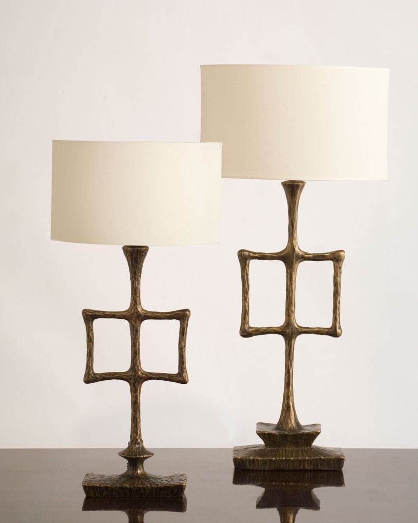 Two brass table lamps with geometric square bases and white cylindrical lampshades on a wooden surface.