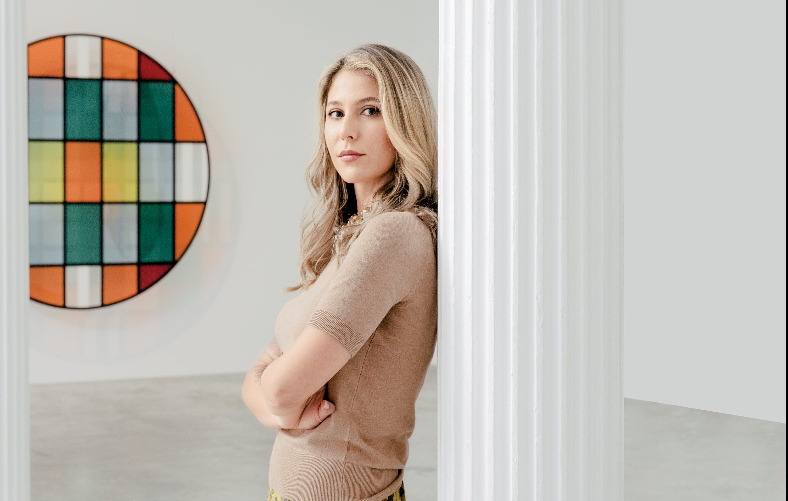 Woman leaning against a column in an art gallery with colorful geometric painting in the background.