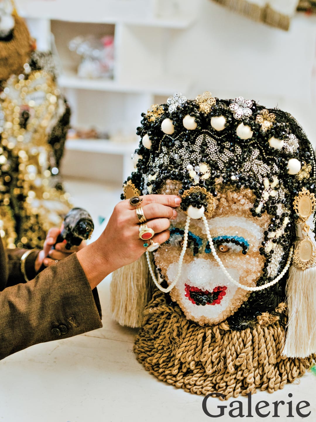 Person applying beads to an ornate mask in an art studio.