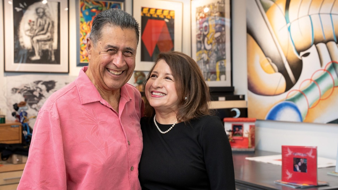 Smiling couple standing together in an art gallery with colorful paintings in the background.