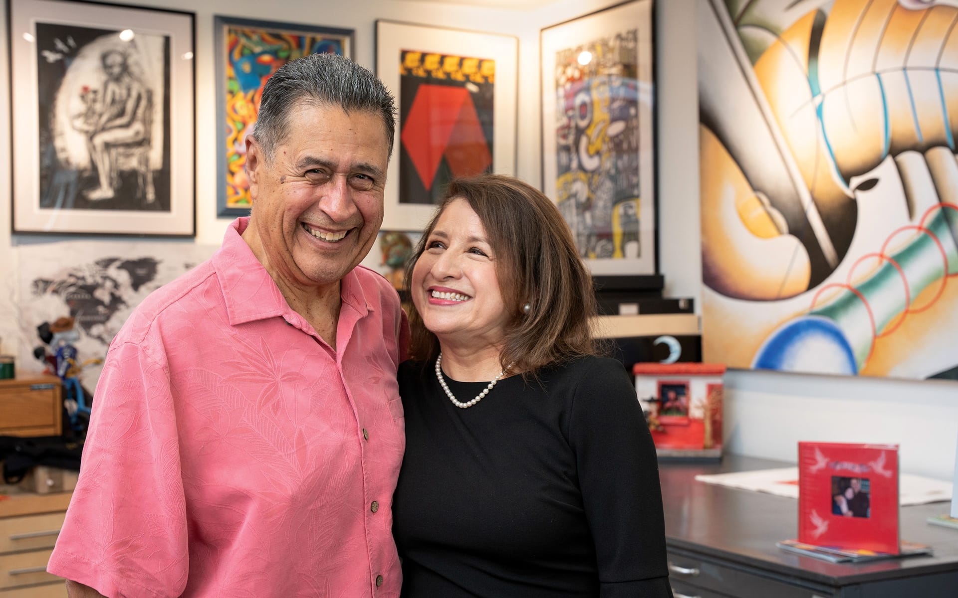 Smiling couple standing together in an art gallery with colorful paintings in the background.