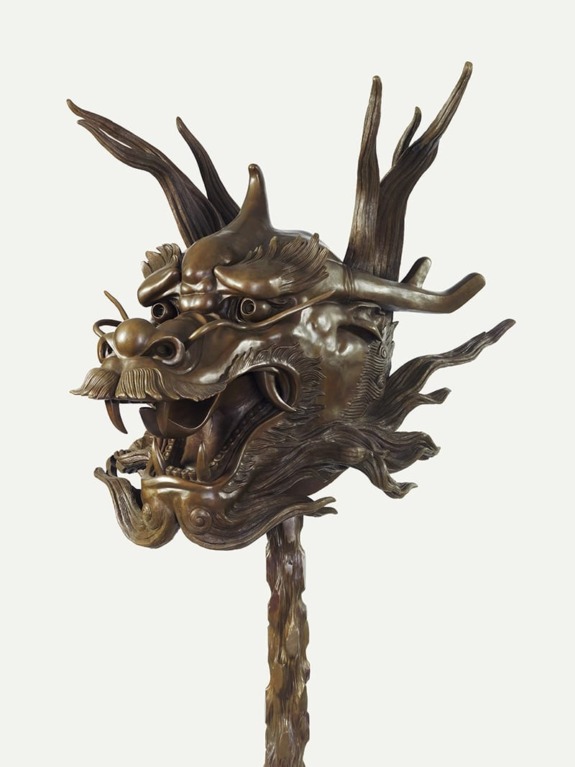 Bronze dragon head sculpture with intricate detailing and expressive facial features, set on a light background.