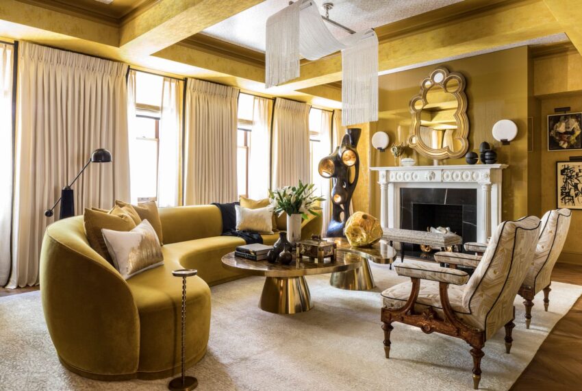 Luxurious living room with gold accents, curved sofa, modern art, elegant mirror, and fireplace surrounded by stylish decor.