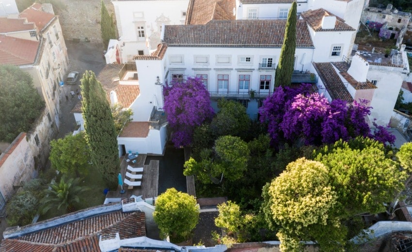 Aerial view of a historic villa with purple bougainvillea and surrounding greenery in a Mediterranean-style setting.